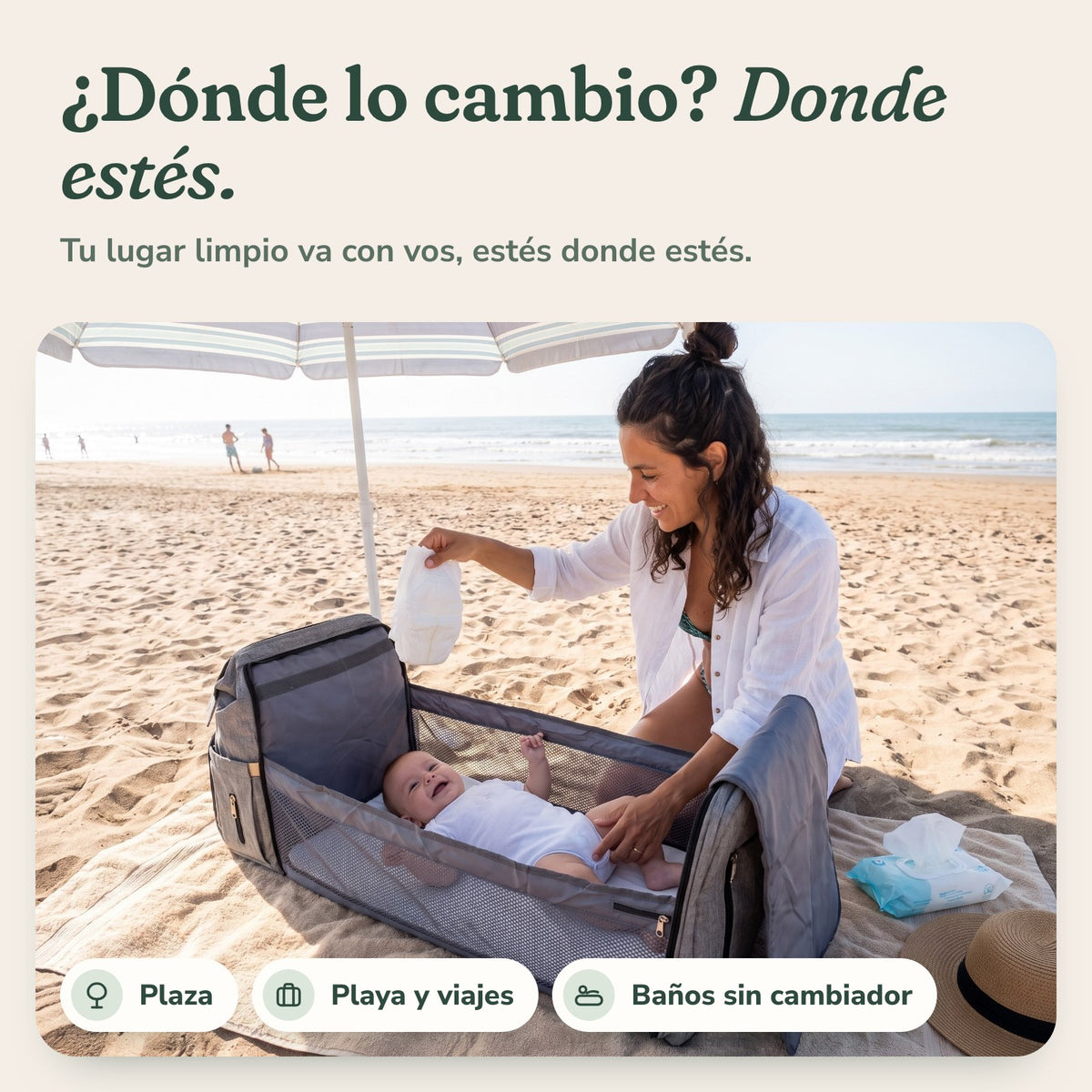 Mamá cambiando al bebé en la playa sobre la mochila Cielú abierta: dónde lo cambio, donde estés