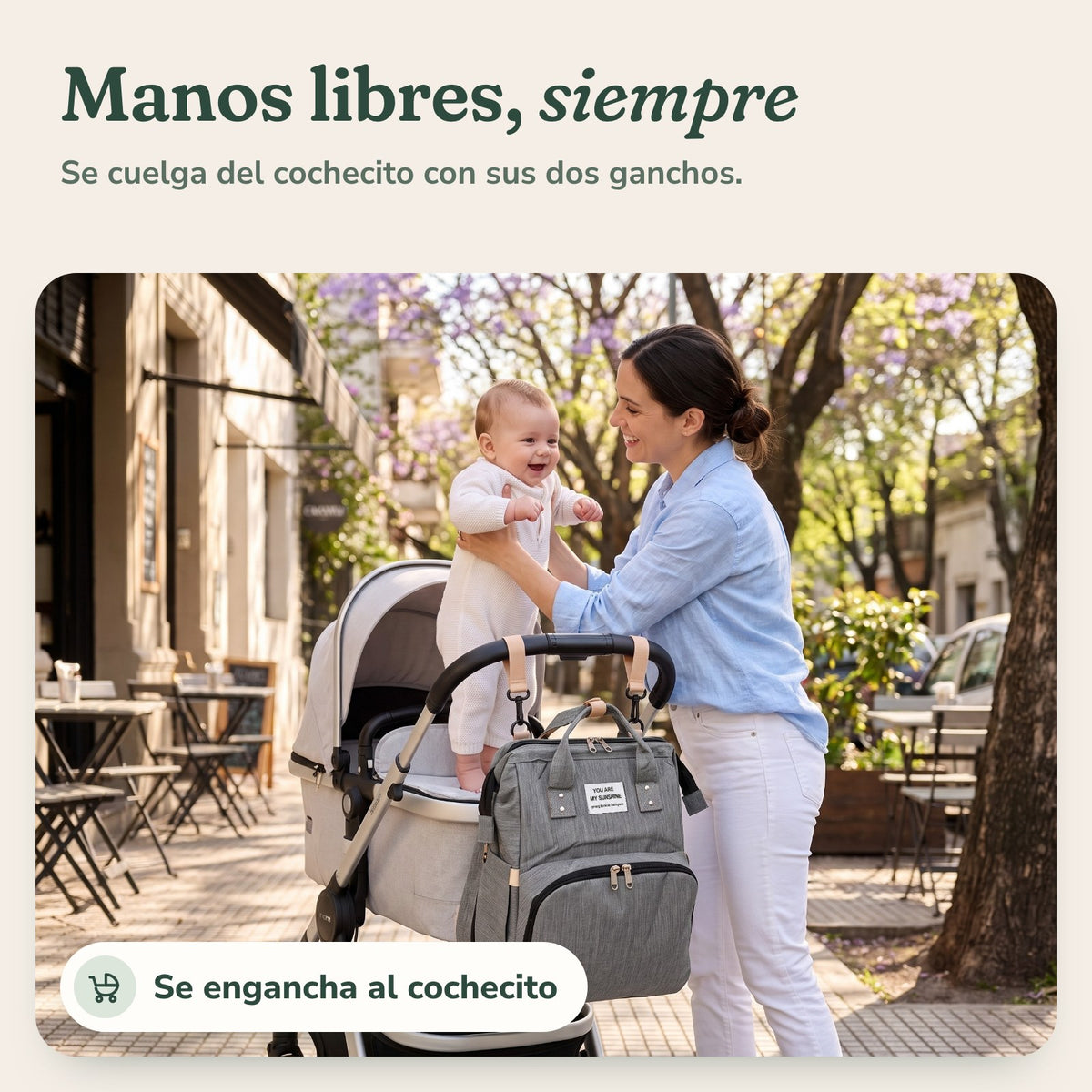 Mochila Cielú colgada del cochecito con sus dos ganchos, mientras la mamá alza al bebé: manos libres