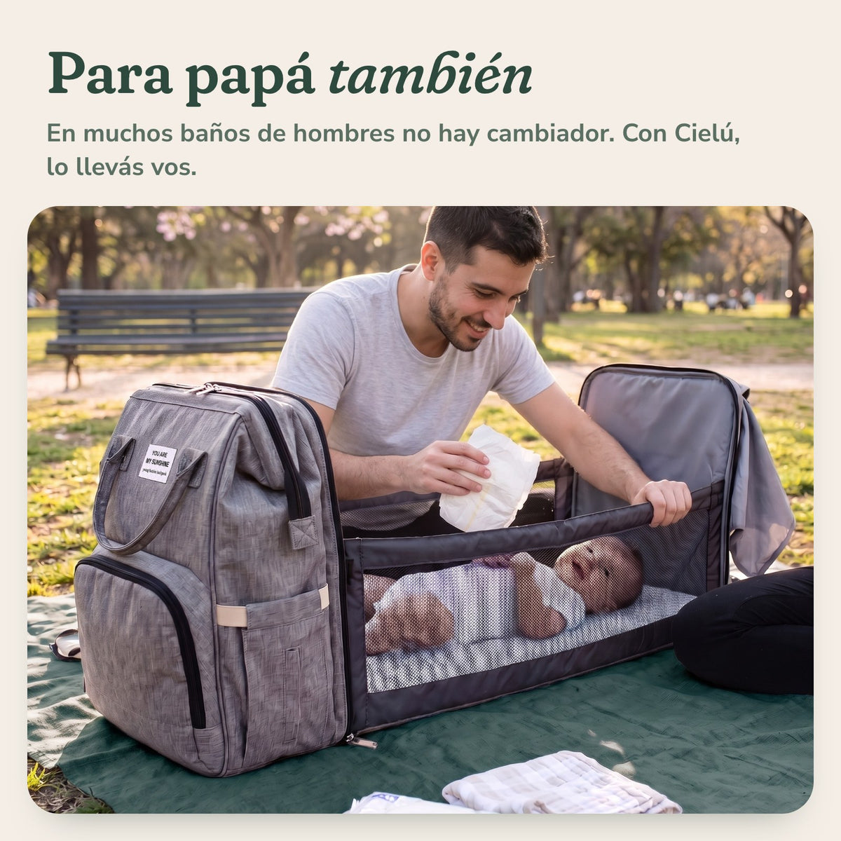 Papá cambiando al bebé en la plaza sobre la mochila Cielú abierta: para papá también